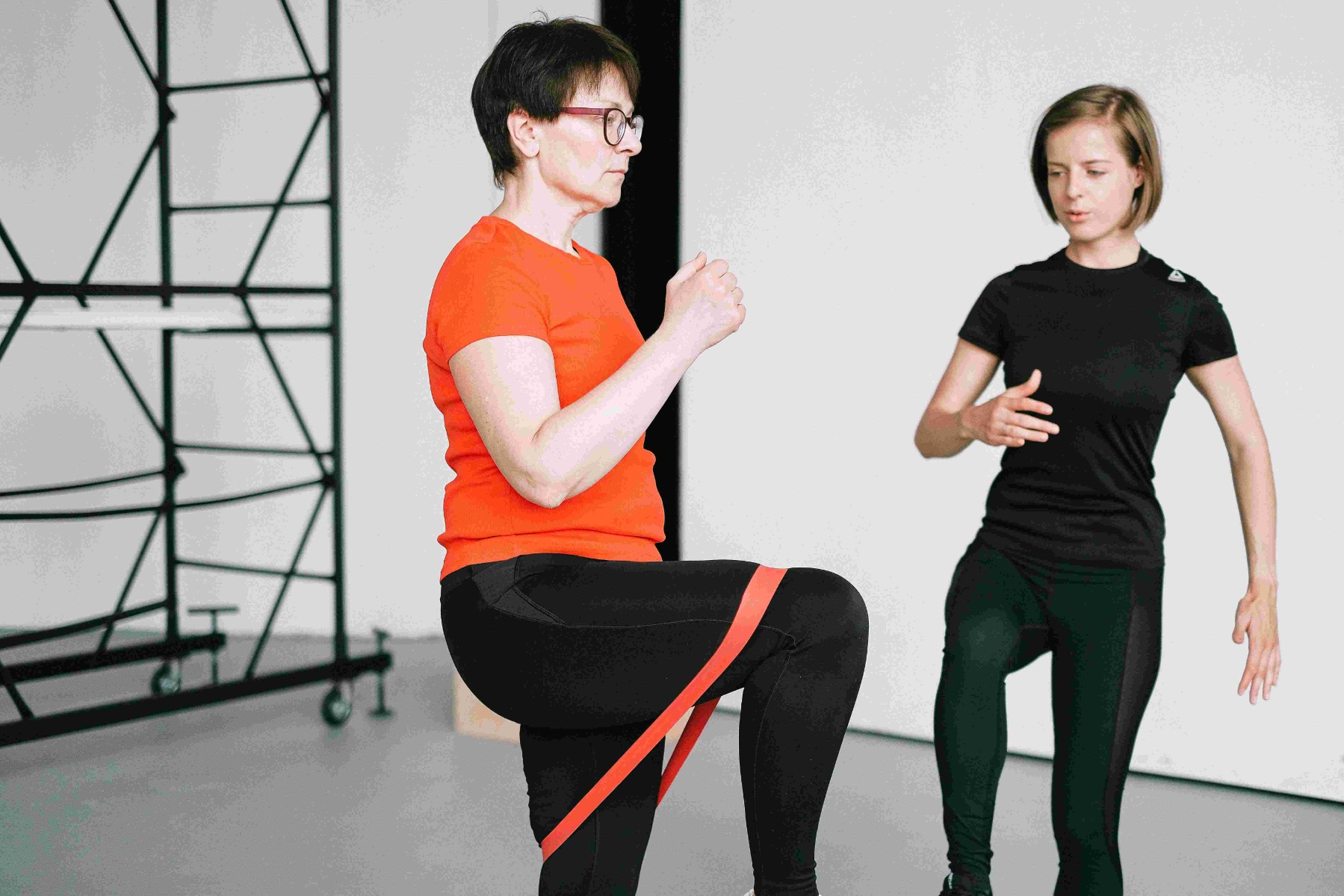 resistance-exercise-bands-clinical-strength-mobility-rehab-training-trimbio Two people performing a knee‑lift exercise with a red resistance band looped around the thighs, demonstrating clinical strength, mobility and rehabilitation training.