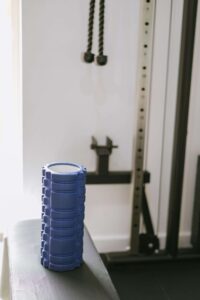 A blue textured foam roller resting on a gym bench beside cable‑machine attachments, showing a physiotherapy recovery tool suitable for mobility work and muscle release.