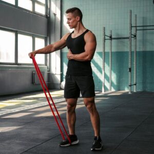 An athlete performing a lateral raise using a resistance exercise band in a gym, demonstrating strength and mobility training suitable for Hyrox preparation.