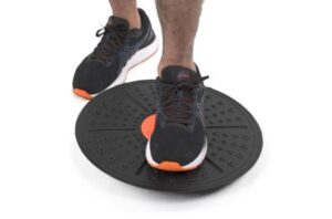 A person standing on a balance board, demonstrating controlled ankle and knee stability training used to treat and prevent injuries while improving balance and proprioception.