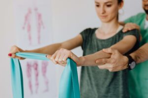 A therapist guiding a patient through an upper‑body resistance‑band exercise, illustrating the type of essential rehabilitation tools physiotherapists commonly rely on in clinical practice.